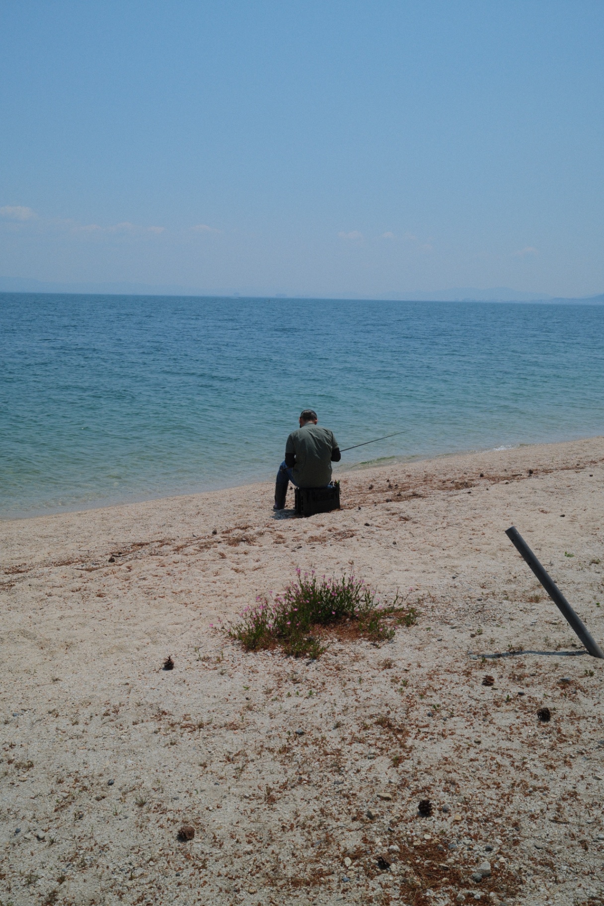 Lone fisherman seated at the edge of a quiet sea