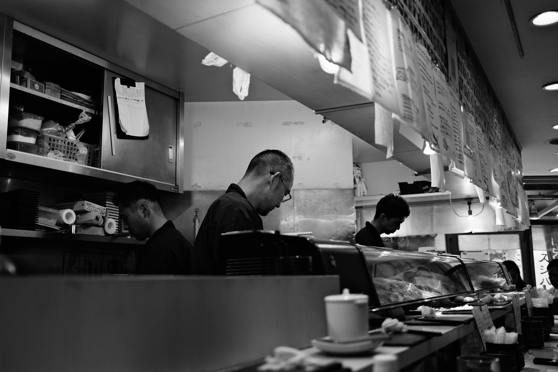 Three men at work behind a sushi counter, black and white